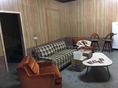 This a pop-up set of a 1970's style basement living room space with wood paneling and brick foundation.	